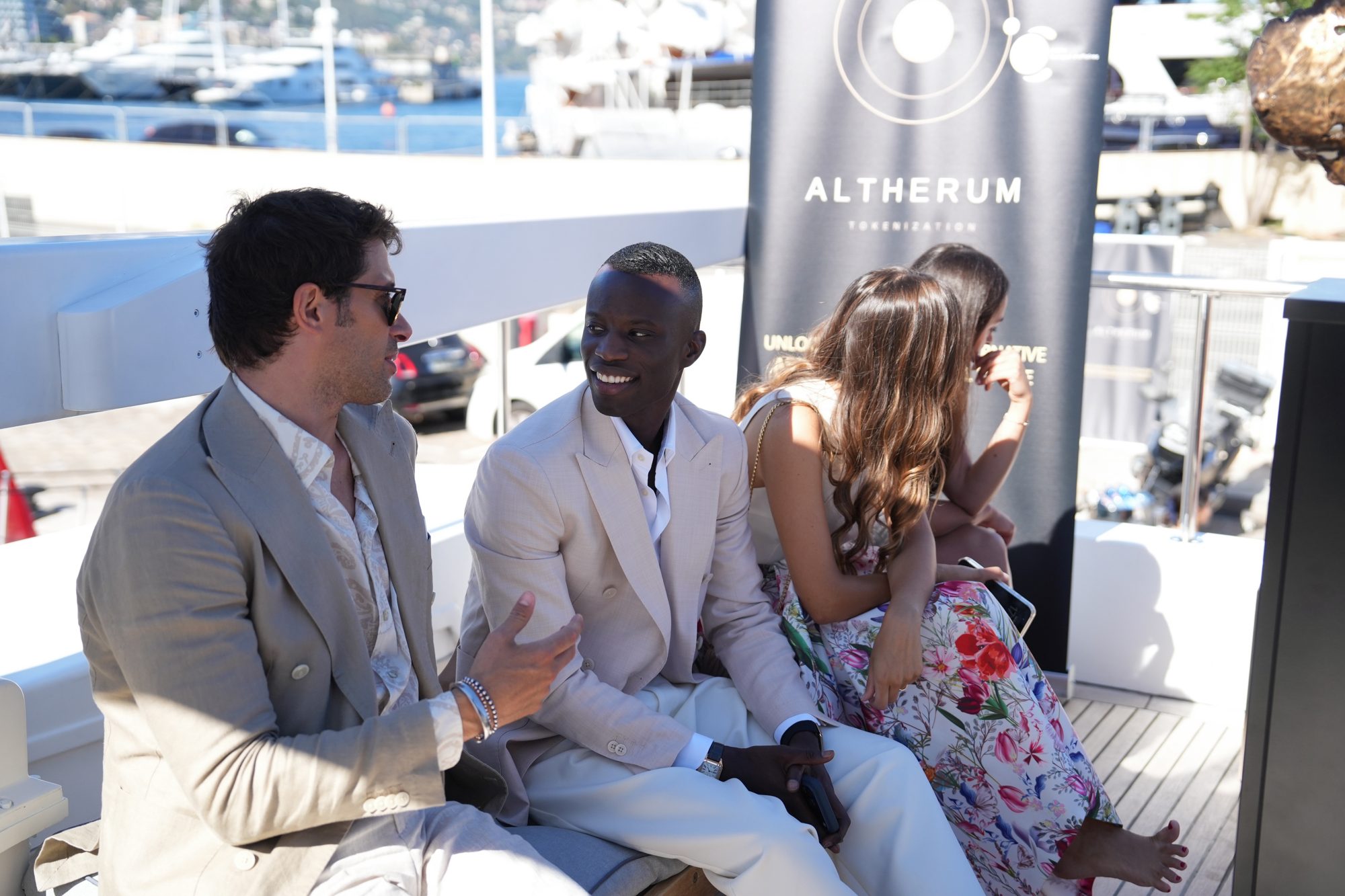 Guests in conversation on deck beside an Altherum Tokenization banner, Monaco marina in the background